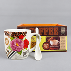 Decorative coffee mug with floral design, spoon, and 'Coffee' themed box on a gray background