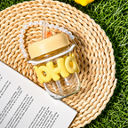 Glass jar with yellow text and accessories on a woven mat with grass in the background