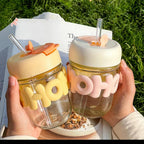 Two clear drink containers with colorful lids and straws held by hands against a grassy background.