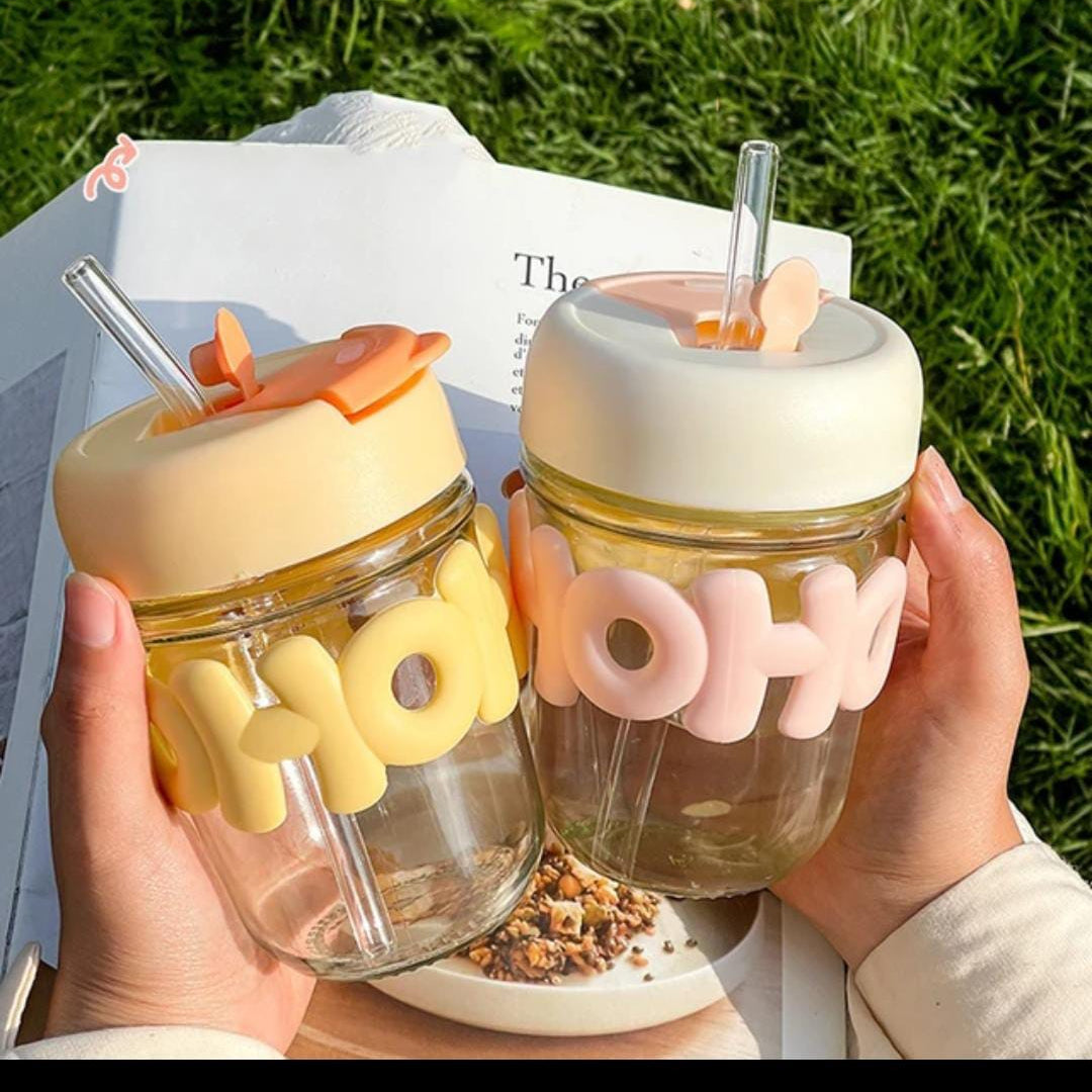 Two clear drink containers with colorful lids and straws held by hands against a grassy background.