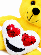 Yellow teddy bear with a heart-shaped pillow featuring red and black sequins on a white background