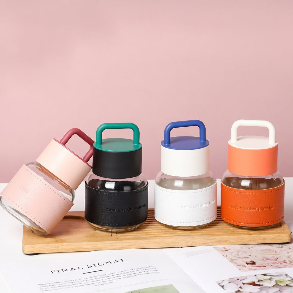 Set of four colorful glass bottles with handles on a wooden stand against a pink background.