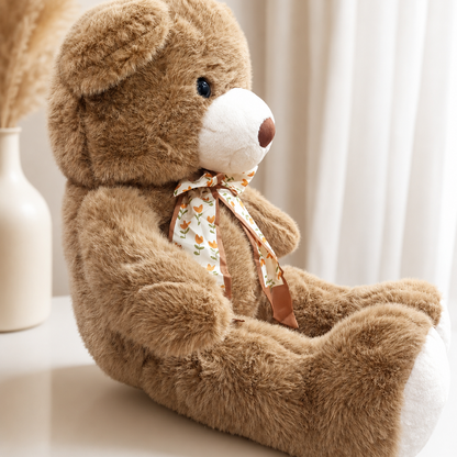 Plush teddy bear seated sideways showing floral bow and white paw pads