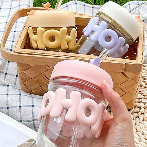 Glass jars with pink and white 'HOH' lid held by a hand, with a picnic basket in the background.