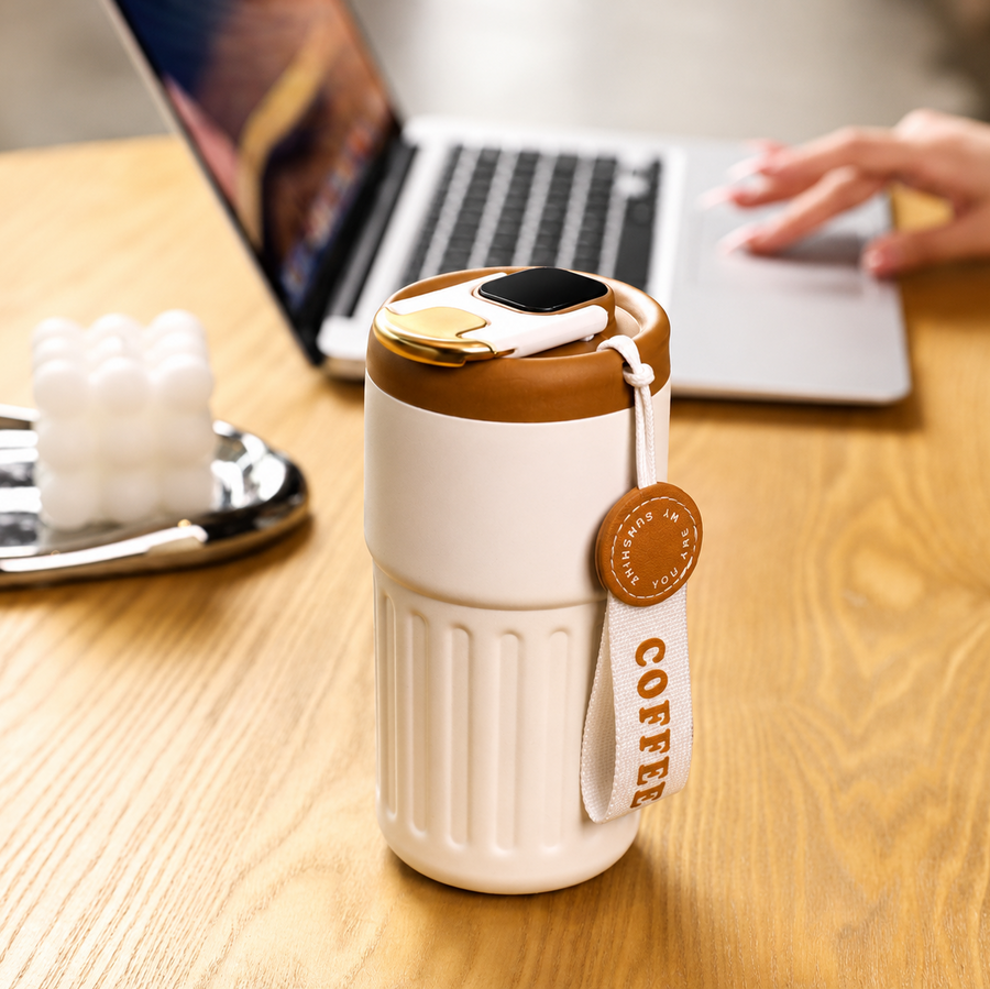 Smart coffee mug with LED display on wooden desk beside laptop and smartwatch