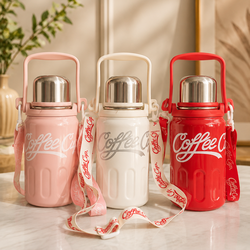 Three insulated coffee thermoses in pink, white, and red, each with a carry handle, stainless steel lid, and branded shoulder strap, displayed on a light marble surface in a warm indoor setting.