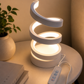 White spiral LED lamp glowing warm light on bedside table with plant and books