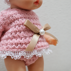 Close-up of a pink knitted dress with a bow and pearl on a plain background